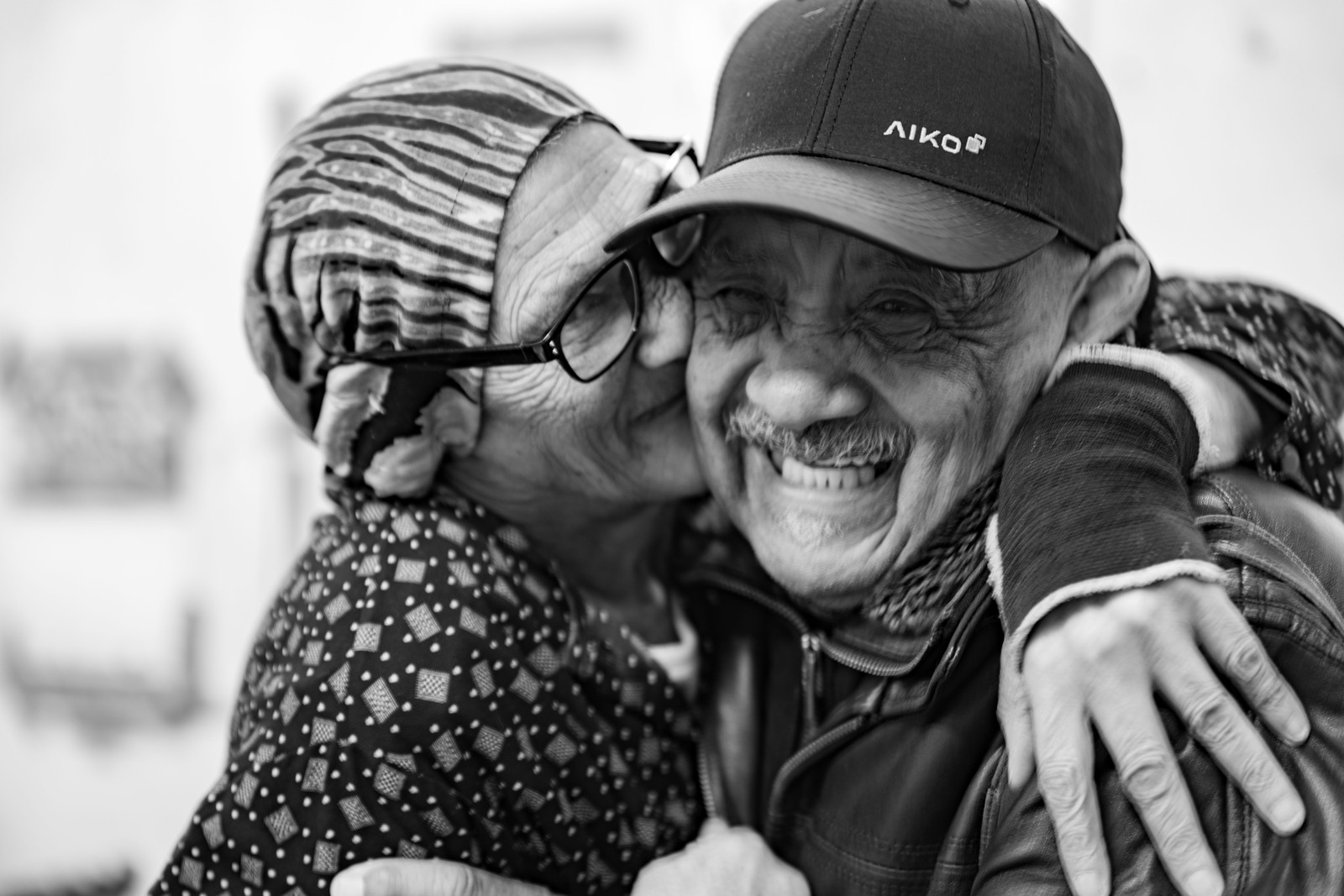 An older woman leaning in to kiss an older man on the cheek, both smiling