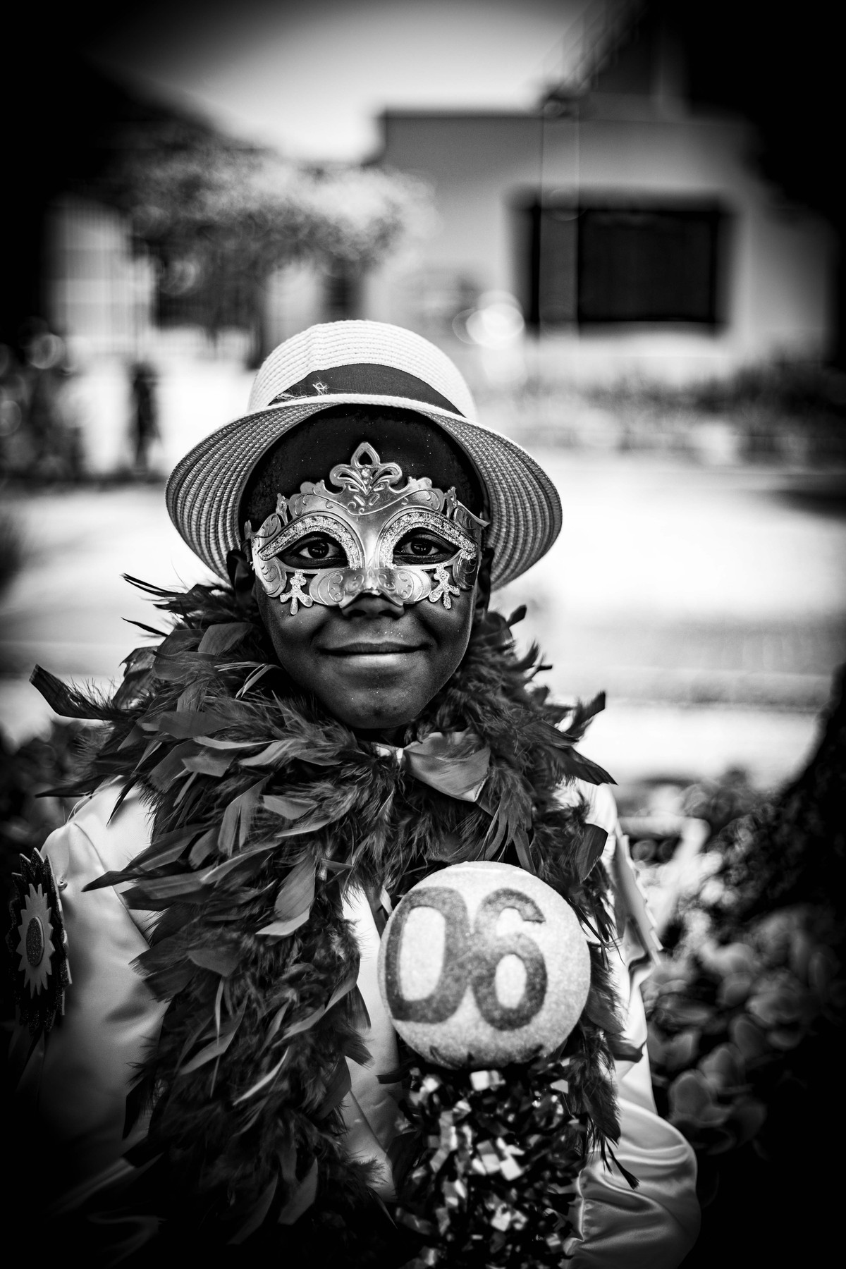 A performer in a painted mask and a feathered collar, wearing a competitor number