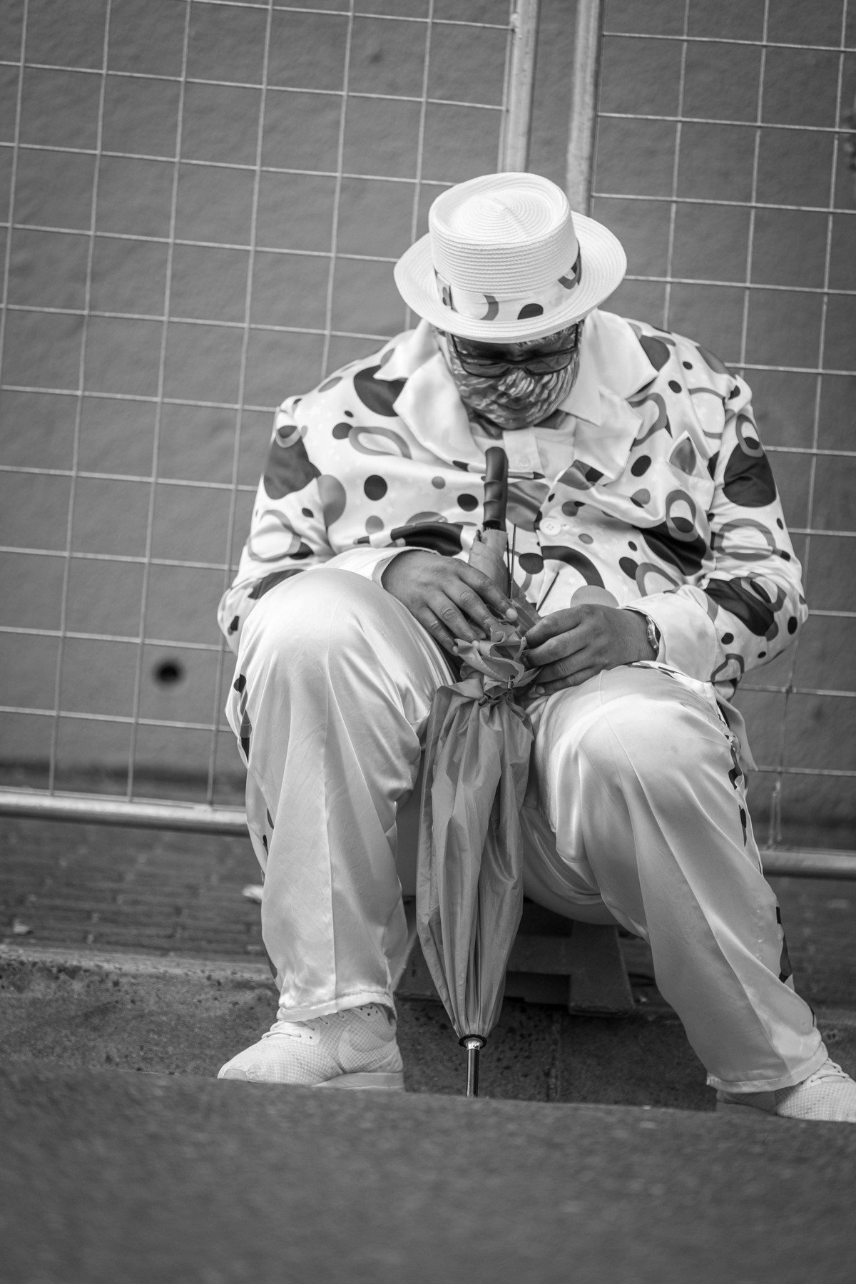 A performer in a straw boater and patterned suit sitting alone with his head bowed