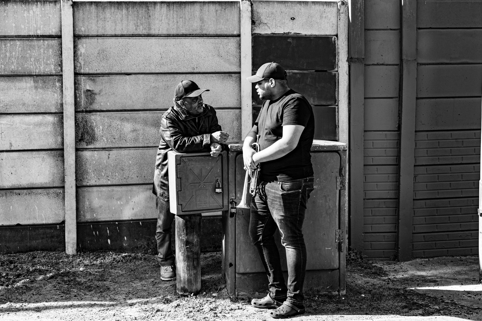 Two men standing by a utility box against a corrugated wall on a Cape Town street