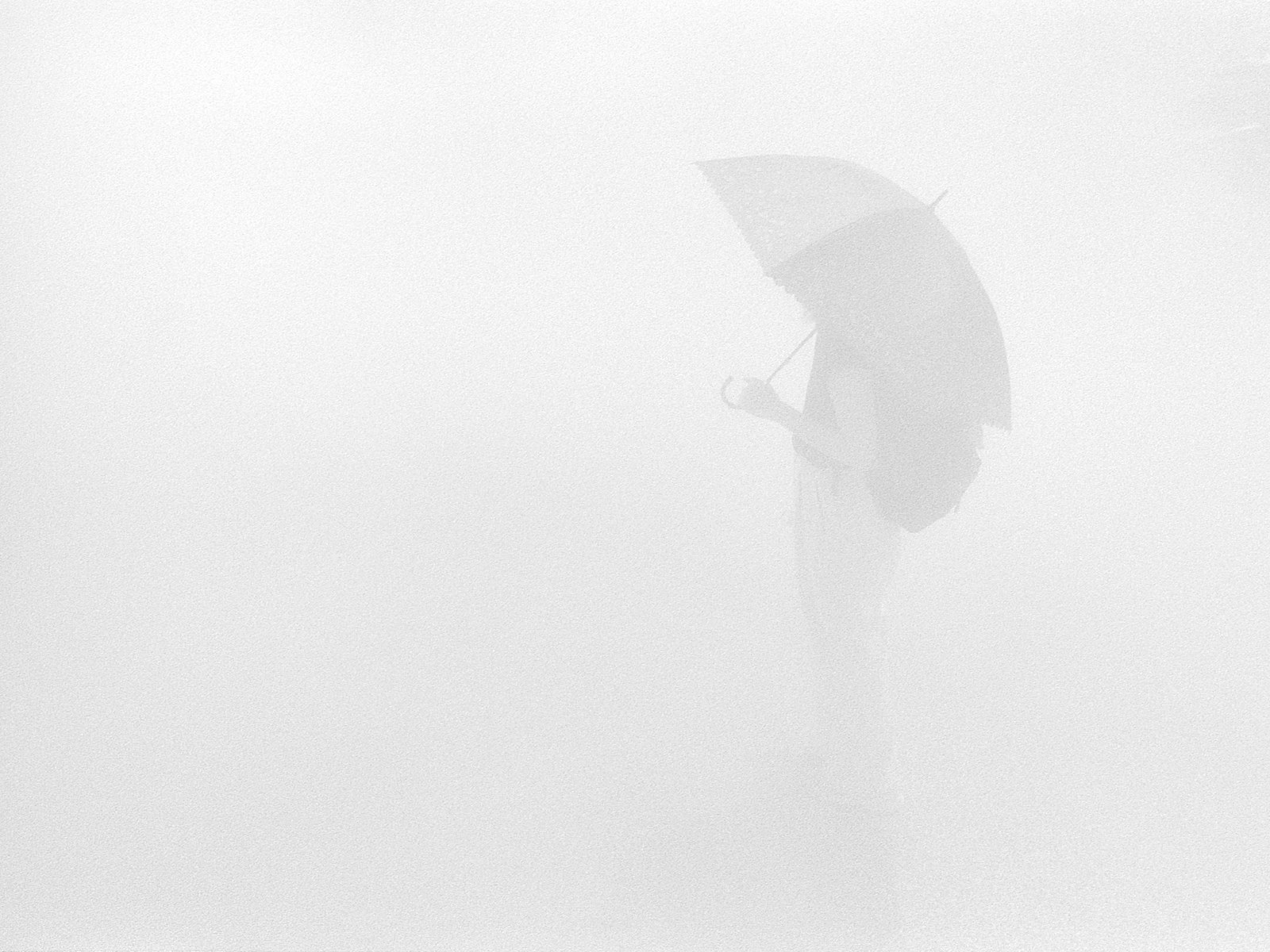 A figure in dense white mist holding an open umbrella, standing to the right of a frame that is otherwise empty white