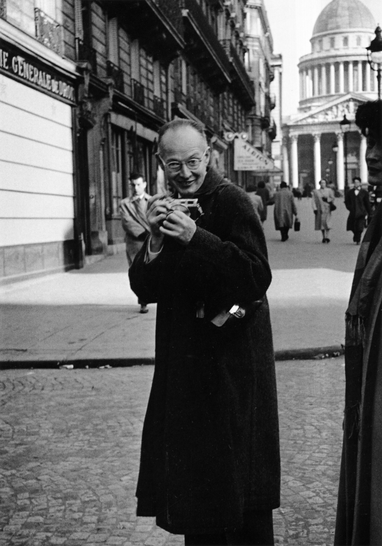 Henri Cartier-Bresson smiling on a Paris street with a Leica in his hands