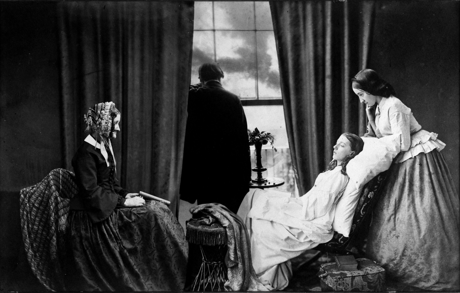 A young woman lying pale on a chair while her mother, sister and father gather around her in a curtained room