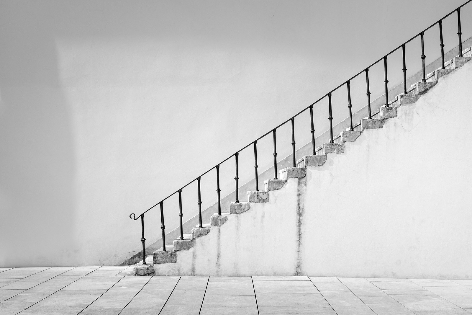 A narrow flight of stone steps climbing a white wall, with evenly spaced black railing posts