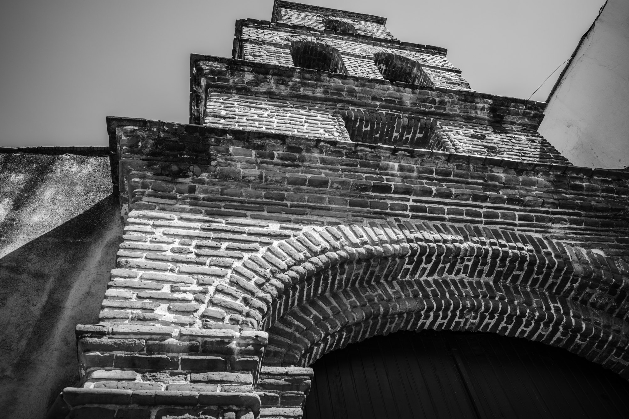 Looking up at the stepped brick gable and arch of an old colonial building against a pale sky