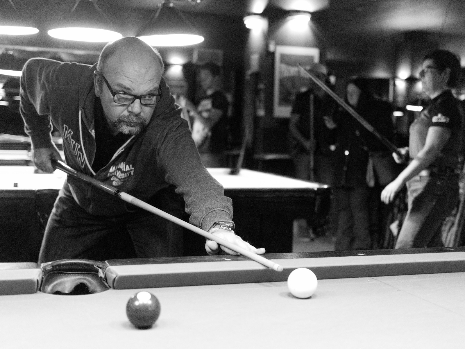 A man leaning across a pool table to take a shot in a crowded hall