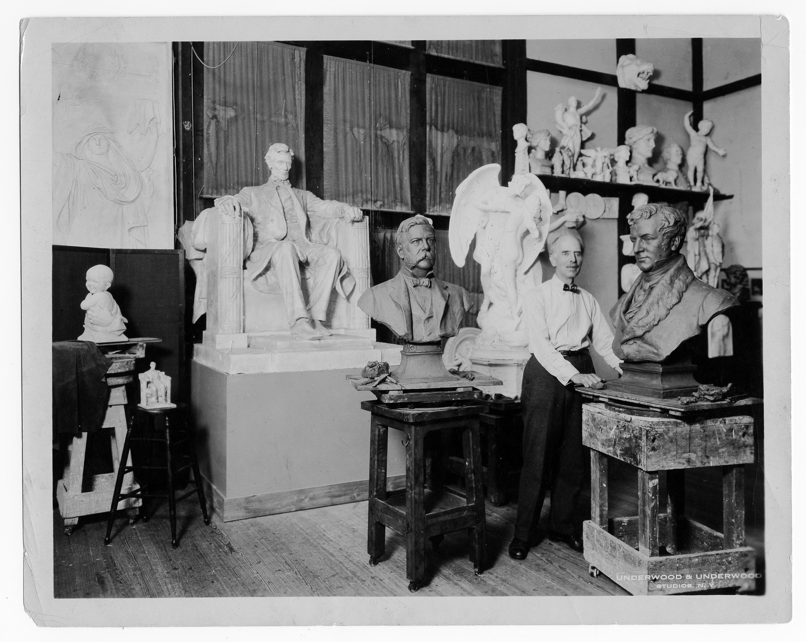 The sculptor Daniel Chester French standing among plaster models and busts in his studio