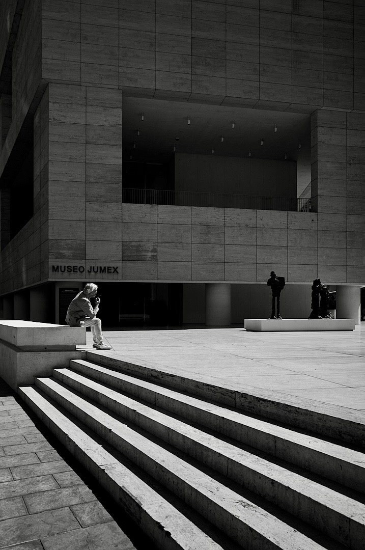 A figure sitting on a bench outside the Museo Jumex in Mexico City, with wide stone steps leading toward them