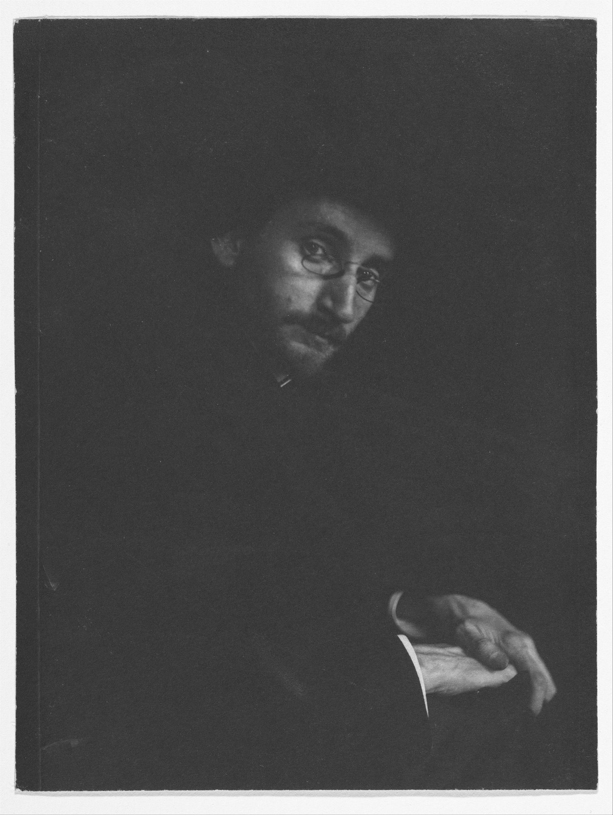 A dark portrait of F. Holland Day, his face and one hand emerging from shadow