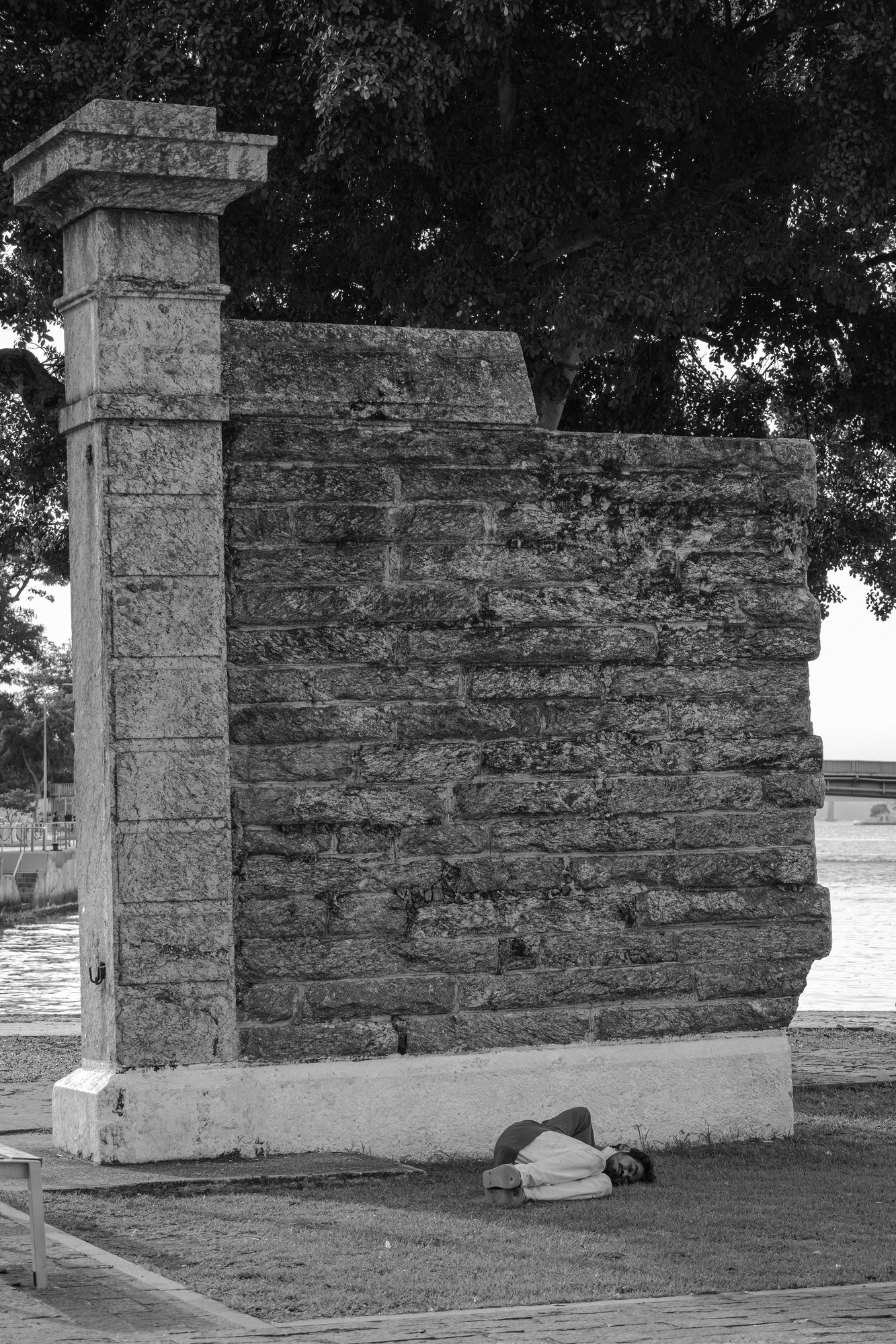 A man sleeps on the grass at the foot of a large old stone wall