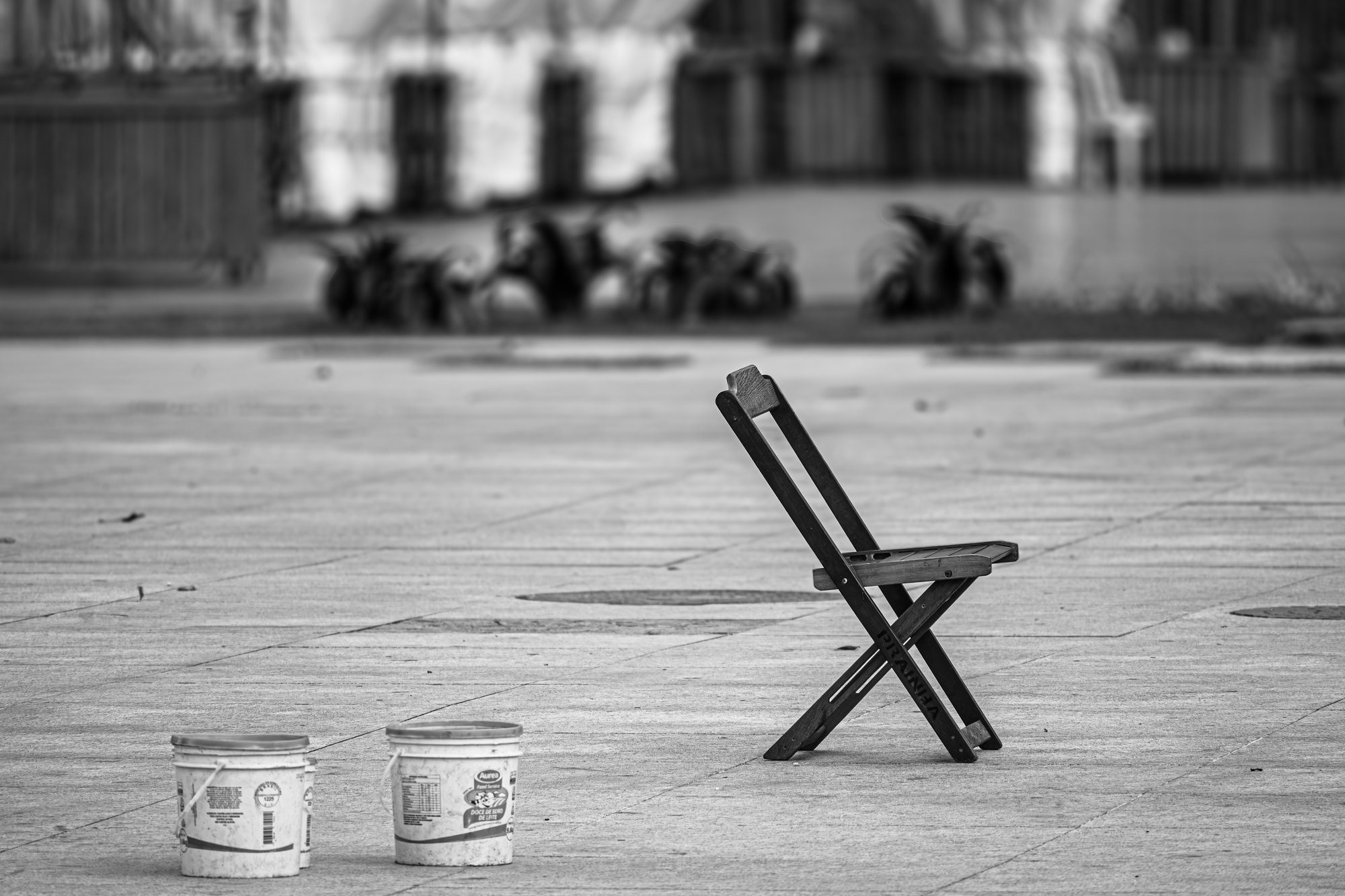An empty folding chair and two plastic buckets left standing on an empty paved square