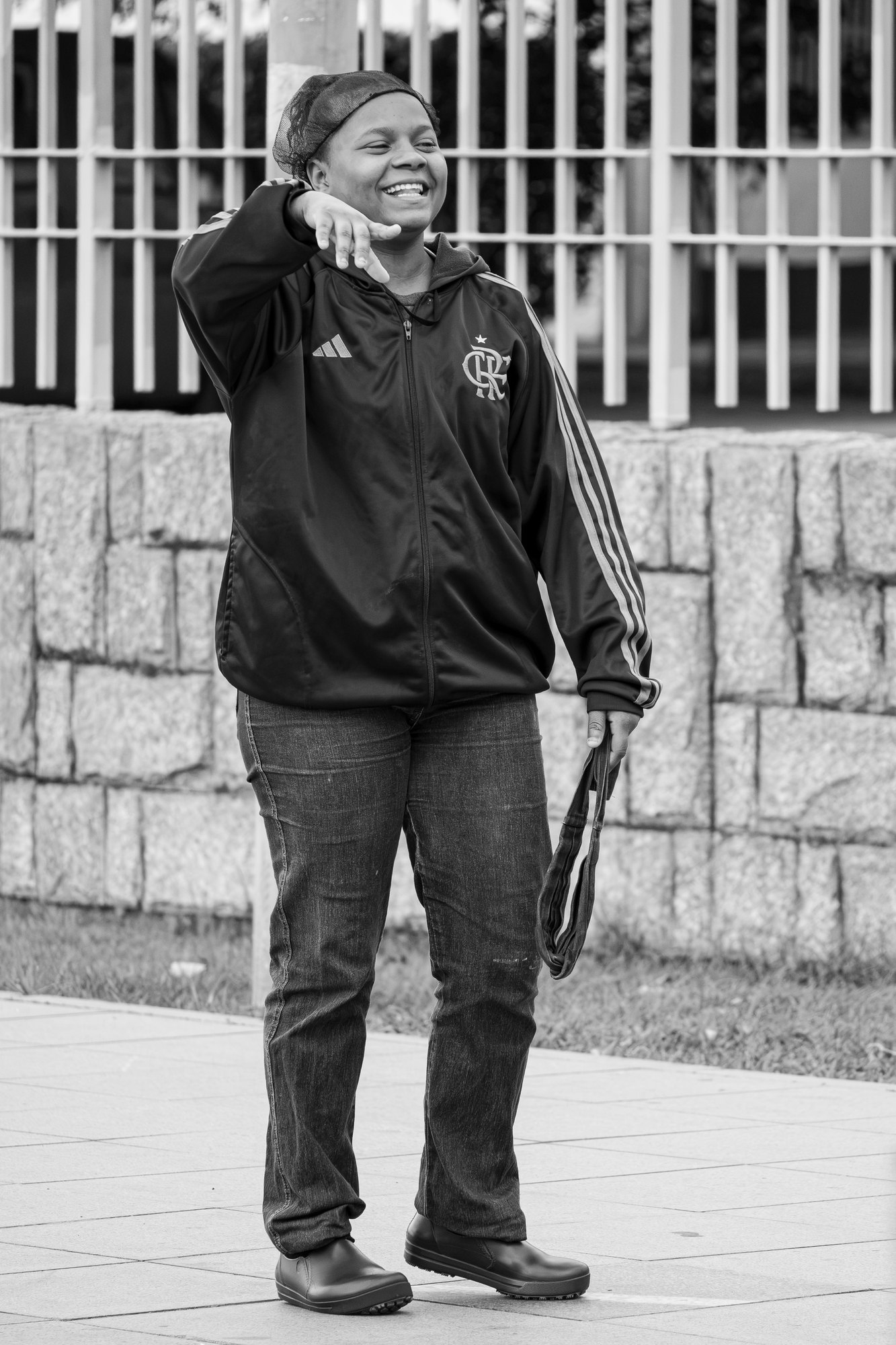A woman in a football tracksuit laughs with her hand raised to her head in front of a stone wall