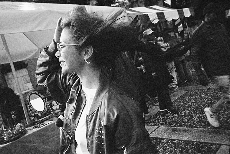A woman at a busy outdoor market with her hair caught in motion, photographed on the QuickSnap Black and White