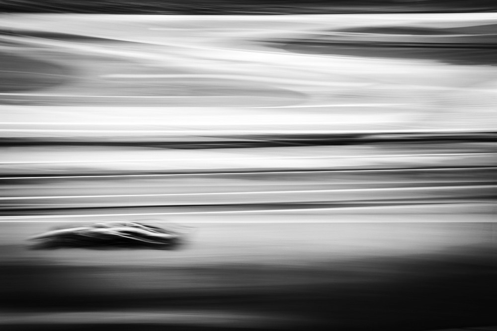 A Formula 1 car reduced to a dark smear against streaked horizontal bands of light in a long panning exposure