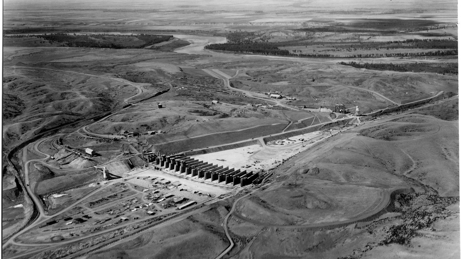 Aerial view of the Fort Peck Dam spillway under construction in Montana in 1936, a long row of concrete piers crossing open prairie