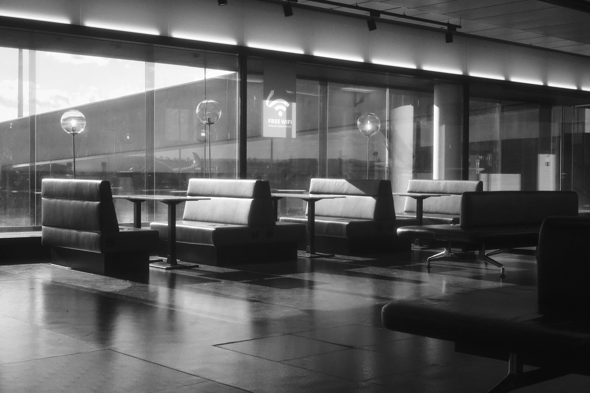 Rows of empty seats and tables in a waiting area in front of a wall of windows, with nobody sitting in them